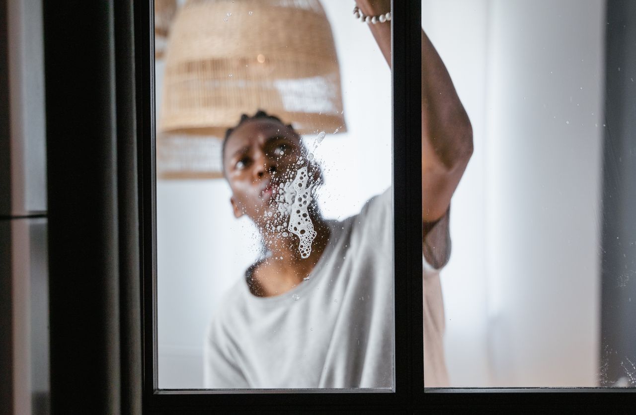 An adult male cleaning a glass window indoors, with attention on household chores and keeping things clean.