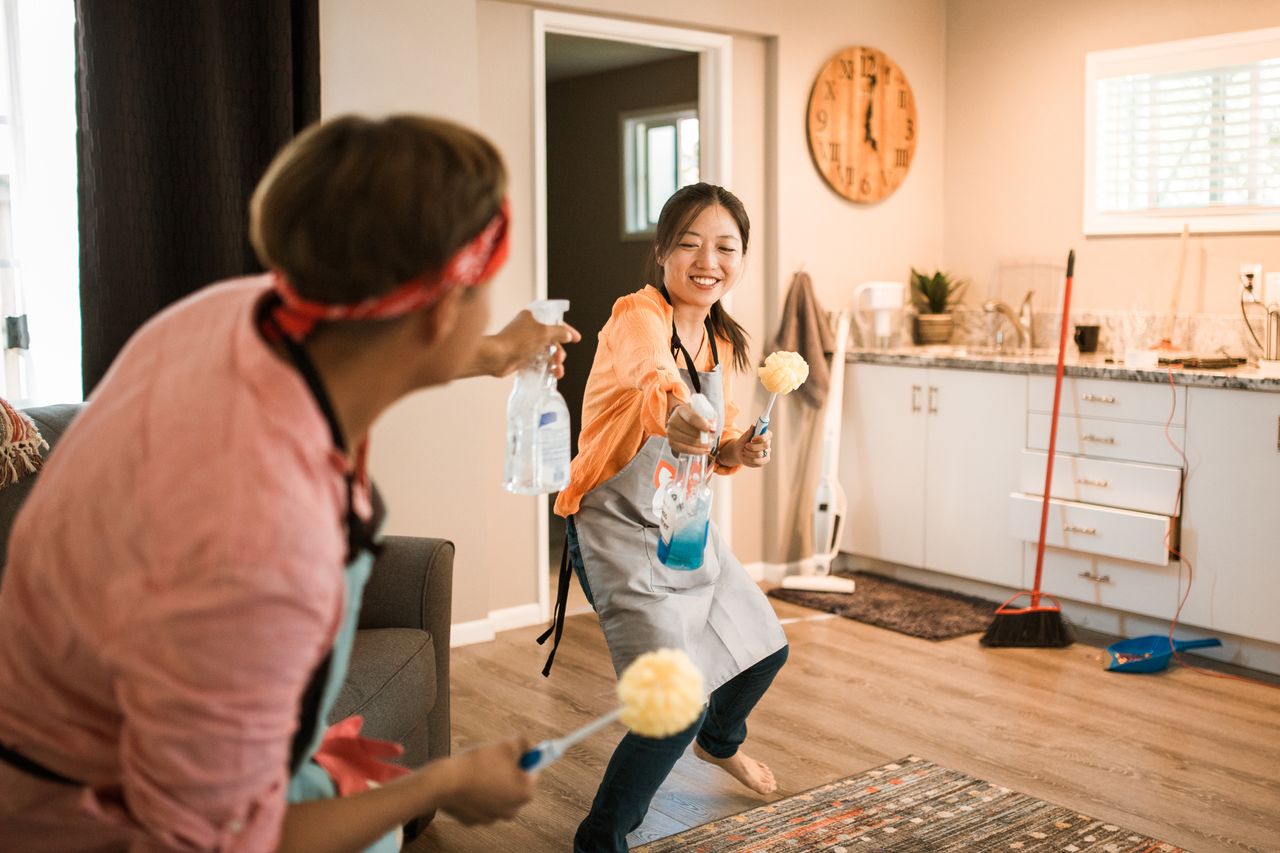 Asian couple having fun while cleaning their home, creating a cheerful atmosphere.
